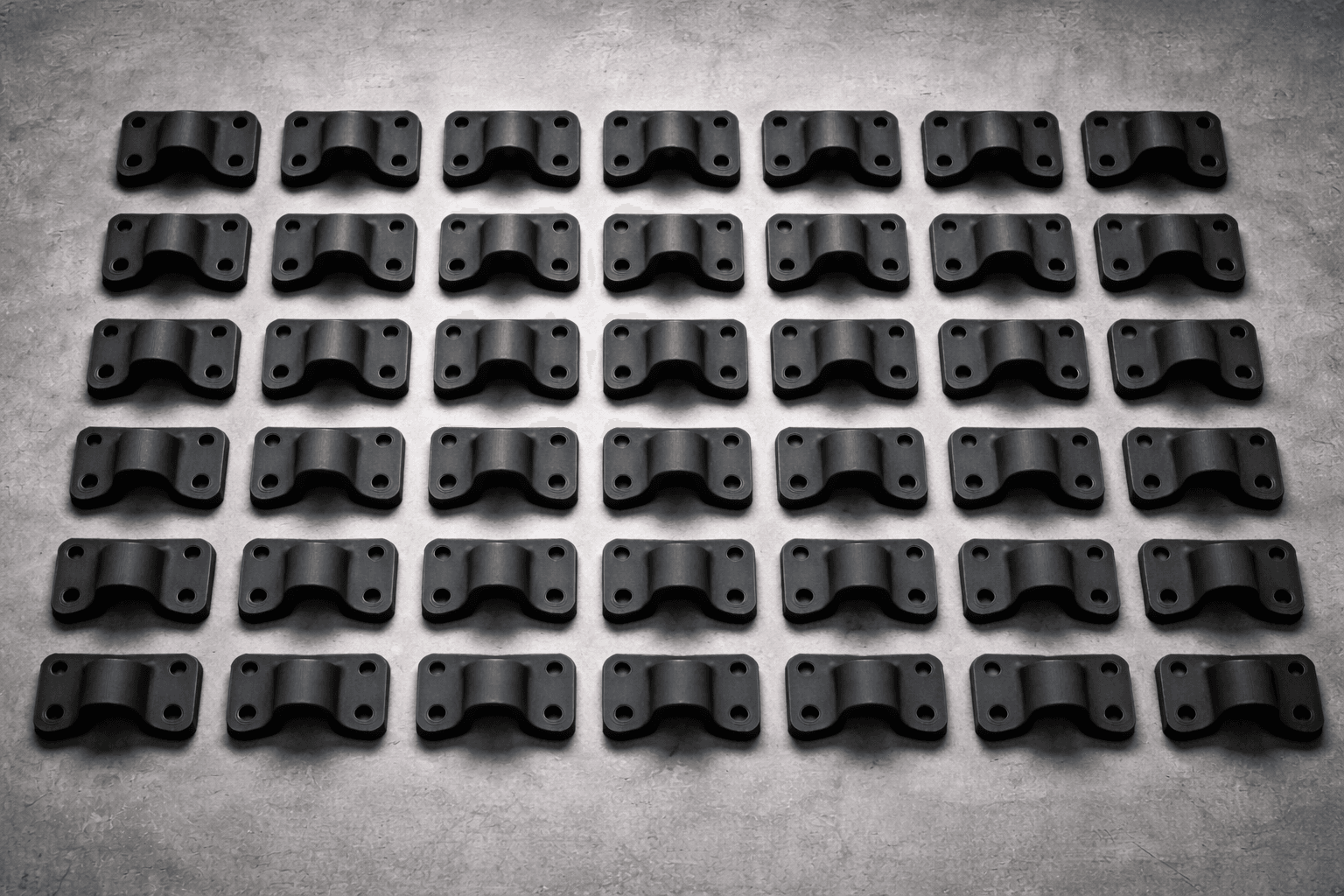 Grid of identical 3D printed carbon-fiber production brackets arranged in neat rows at TAKT 3D San Diego